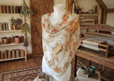 Pañuelo o chal artesanal con estampado natural de hojas en tonos ocres y tierra expuesto en un maniquí