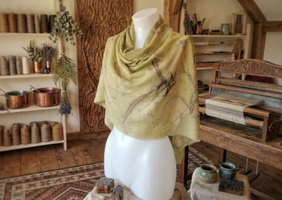 Chal de algodón o lino hecho a mano en tono verde oliva suave, colocado sobre un maniquí en un taller artesanal