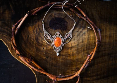 Gargantilla tejida en macramé con una piedra central de color naranja o coral sobre fondo de madera